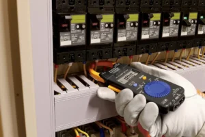 Electrician using HIOKI CM3289 True RMS clamp meter to measure motor current in industrial control panel